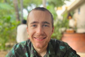 David Craig smiles, wearing a green shirt against a leafy background